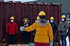 Instruktør i gul jakke og hjelm underviser en gruppe deltakere utendørs i snøvær.
